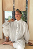 Model wearing Cropped Poet Blouse in White and Cadence Pants in White, sitting in wooden doorway, with trees in the background