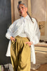 Model wearing Long Poet Blouse in White and Cadence Pants in Dijon in front of wooden doorway to grey building