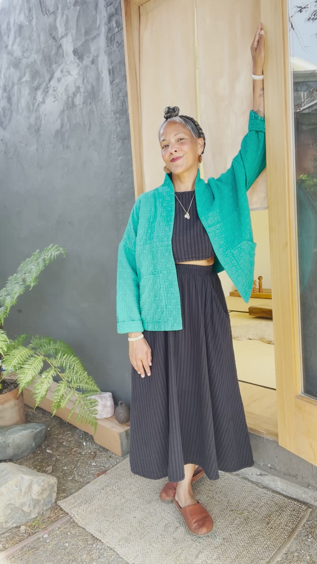 Oona Cardigan in Ocean on model in front of grey building. Model cuffs sleeves and puts hands in pockets.