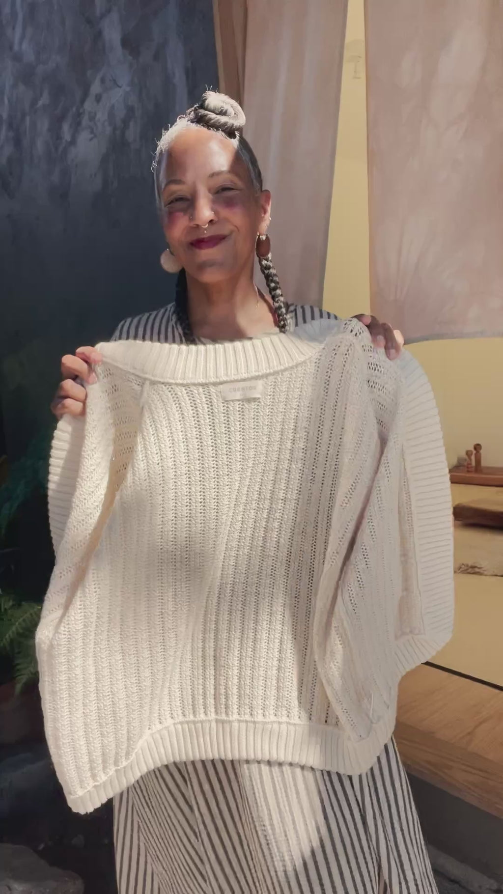 Video of model putting on Maeva Cardigan in Biscuit in front of grey building