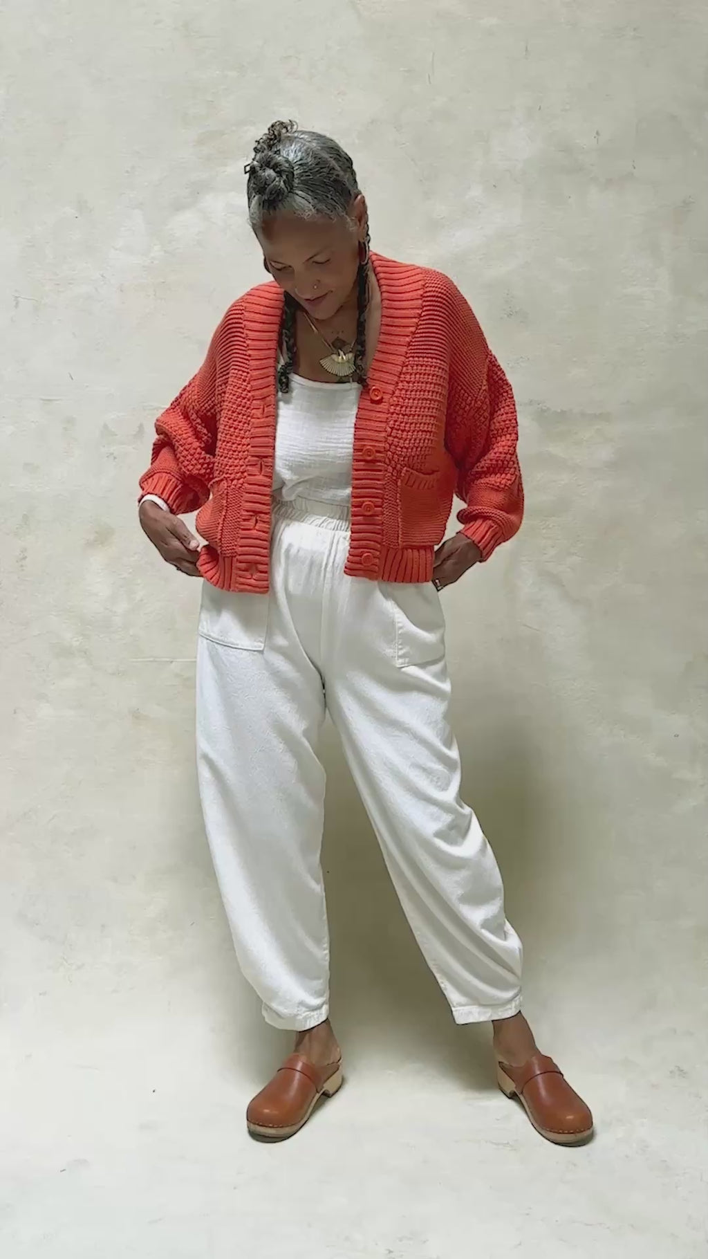 Video of model wearing Lino Cardigan in Tomato and Cadence Pant in White, slowly turning around in front of white background