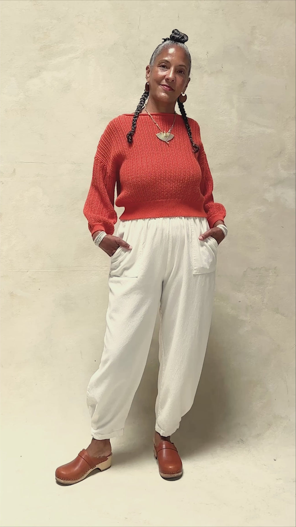 Video of model wearing Lana Sweater in Tomato and Cadence Pant in White, slowly turning in front of white background