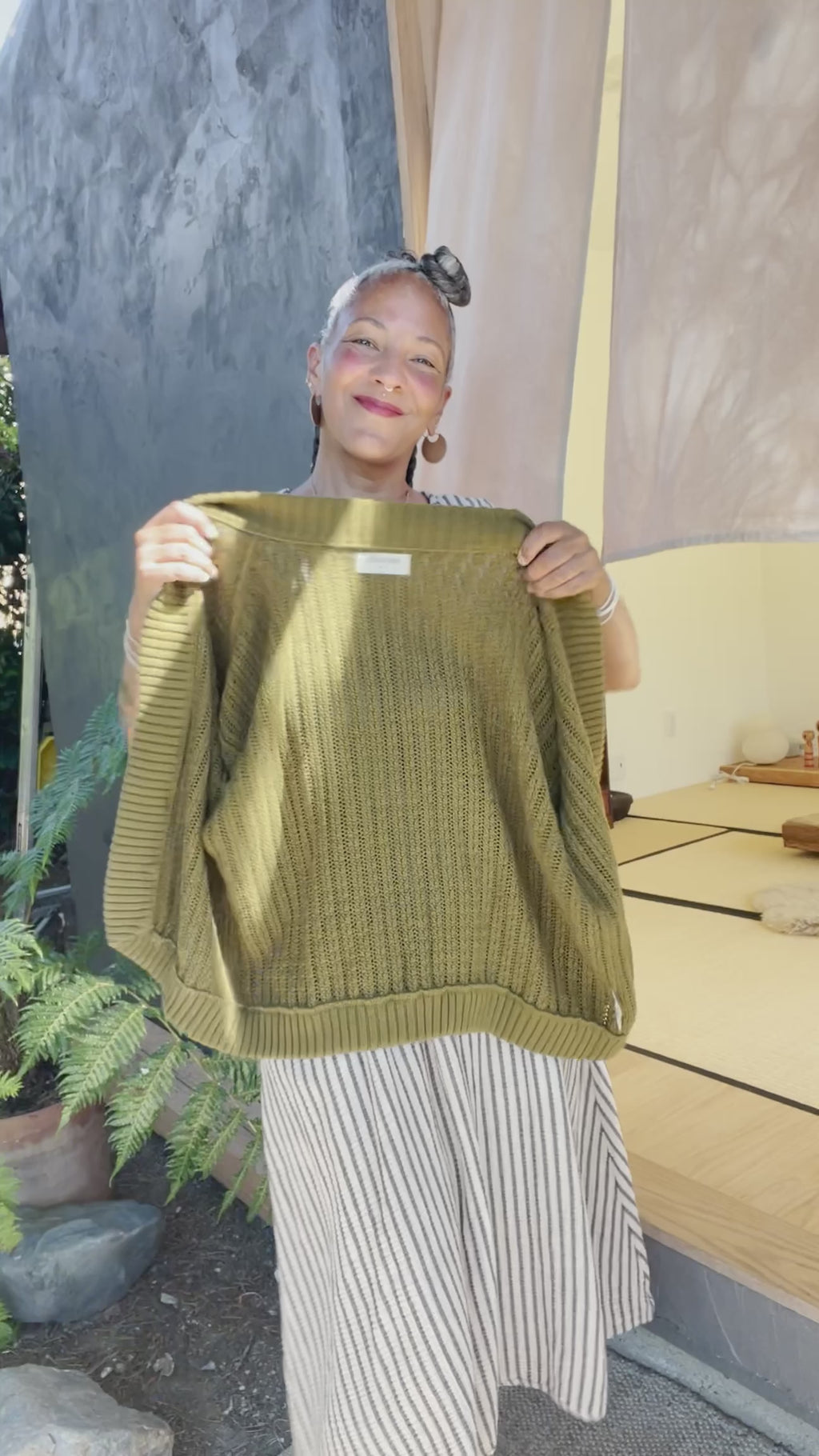 Video of model wearing Noa Stripe Top and Fawn Stripe Skirt, both in Oat, putting on Maeva Cardigan in Fennel in front of grey building