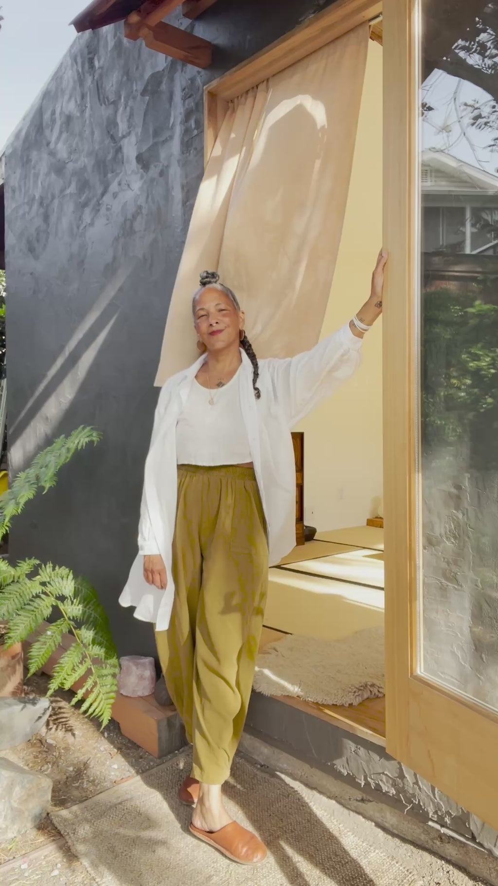 Video of model wearing Long Poet Blouse in White, Minnie Tank in White, and Cadence Pants in Dijon. Video shows model buttoning up shirt, cuffing sleeves, and putting hands in pants pockets.