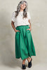Front view of model wearing Rosey Sweater in Biscuit and Fawn Poplin Skirt in Fern, standing with hands in skirt pockets in front of white background