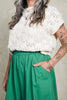 Close up of model wearing Rosey Sweater in Biscuit and Fawn Poplin Skirt in Fern, standing with hand in skirt pocket in front of white background
