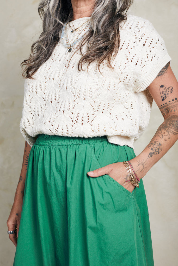 Close up of model wearing Rosey Sweater in Biscuit and Fawn Poplin Skirt in Fern, standing with hand in skirt pocket in front of white background