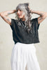 Model wears Rosey Sweater in Black and Cadence Pant in White, standing with hands on head in front of white background