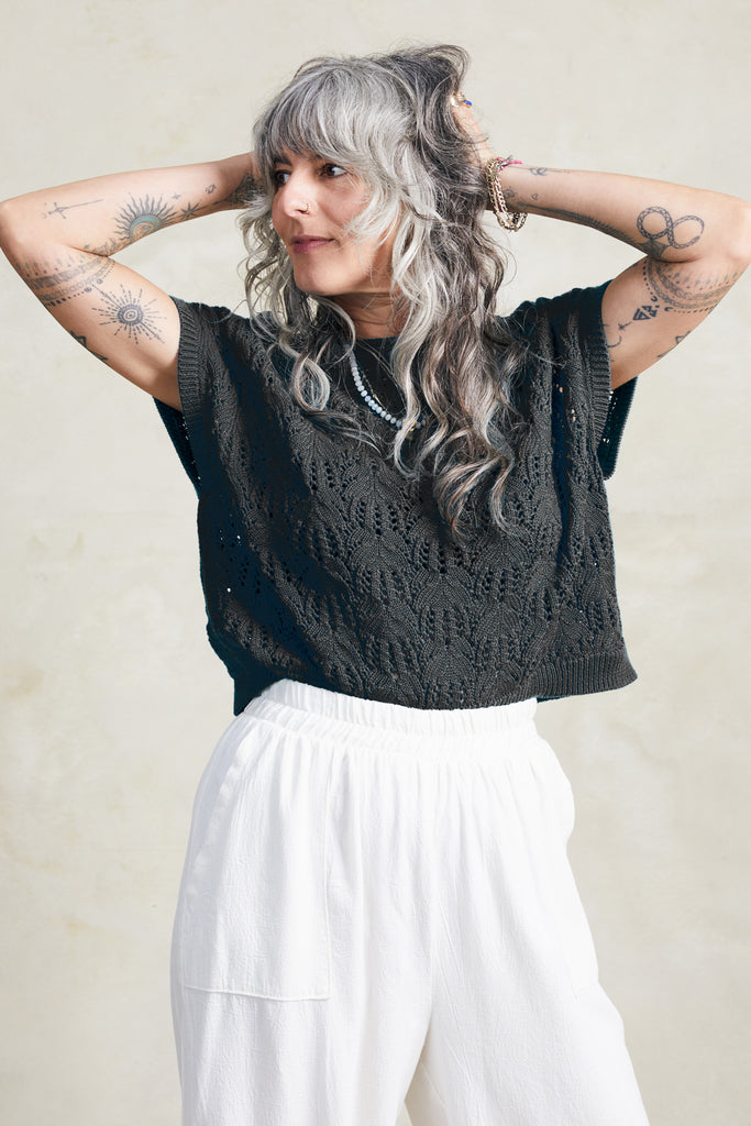 Model wears Rosey Sweater in Black and Cadence Pant in White, standing with hands on head in front of white background
