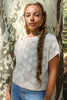 Model wearing Rosey Sweater in Biscuit and light wash jeans standing in front of brown and white tree trunk