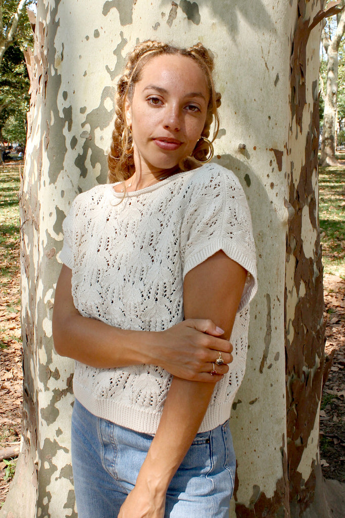 Model wearing Rosey Sweater in Biscuit and light wash jeans standing in front of brown and white tree trunk