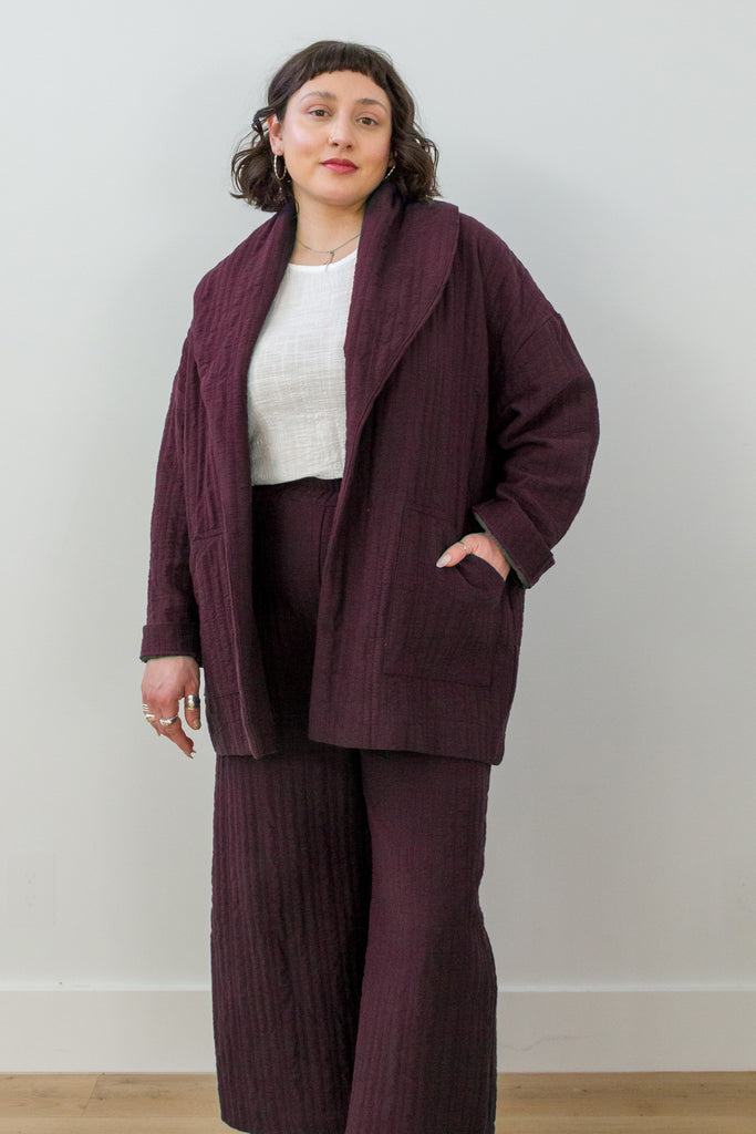 Front view of model wearing Sadie Coat in Burgundy, Ayana Top in White, and Dover Pant in Burgundy, with one hand in pocket in front of white background
