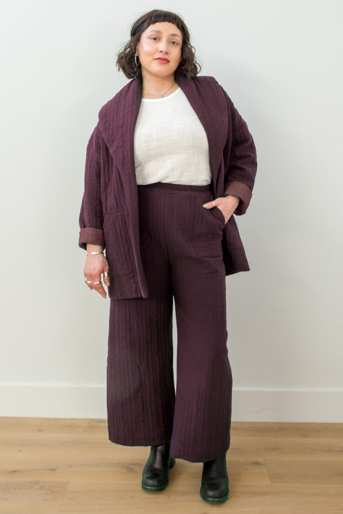 Front view of model wearing Sadie Coat in Burgundy, Ayana Top in White, and Dover Pant in Burgundy, with one hand in pants pocket in front of white background