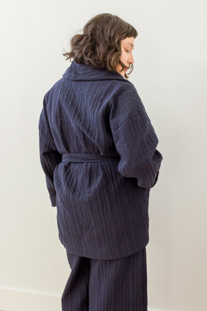 Back view of model wearing Sadie Coat and Dover Pant (both in Indigo) in front of white background