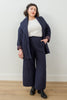 Front view of model wearing Sadie Coat in Indigo, Ayana Top in White, and Dover Pant in Indigo, with one hand in pants pocket in front of white background