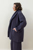Side view of model wearing Sadie Coat in Indigo and Dover Pant in Indigo, with one hand in pocket in front of white background