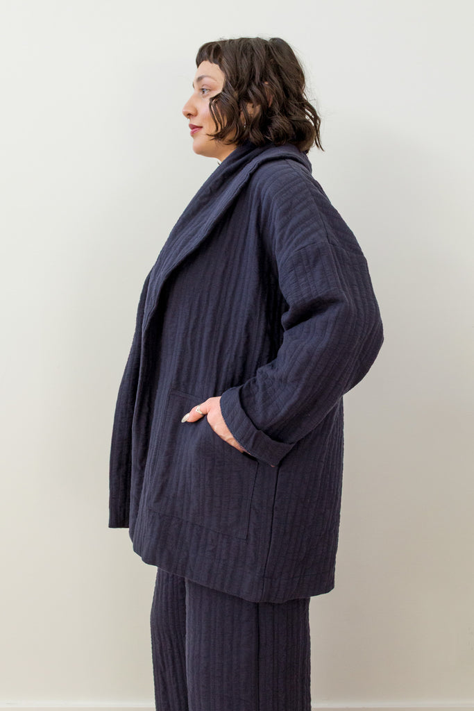 Side view of model wearing Sadie Coat in Indigo and Dover Pant in Indigo, with one hand in pocket in front of white background