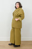 Side view of model wearing Sadie Coat in Fennel with the belt around the waist, Ayana Top in White, and Dover Pant in Fennel, with one hand in jacket pocket in front of white background