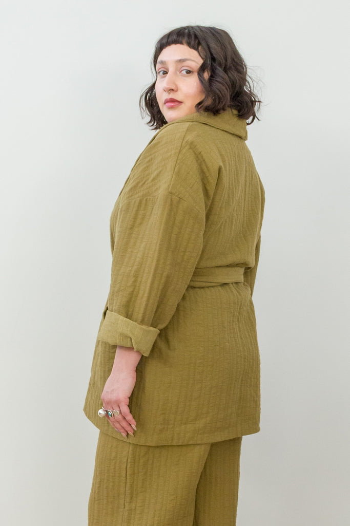 Side view of model wearing Sadie Coat in Fennel with the belt around the waist and Dover Pant in Fennel,  in front of white background