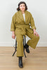 Front view of model wearing Sadie Coat in Fennel with the belt around the waist, Ayana Top in White, and Dover Pant in Fennel, sitting on a black stool in front of white background