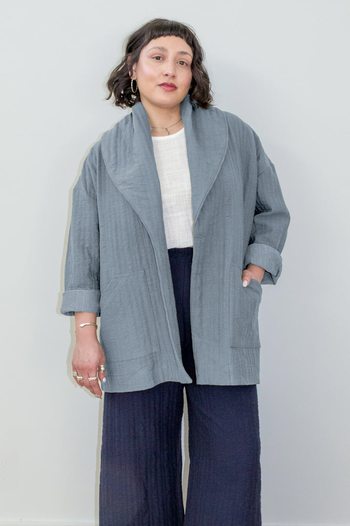 Sadie Coat in Stone on model. Woman wearing a light blue jacket over a white top and dark pants on a plain background.