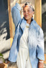 Woman wearing a stone blue Sadie Coat - textured jacket over a white top and pants, standing outdoors.
