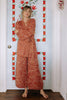 Model wearing Stevie Sweater and Sofie Sweater Pants, both in Rust Melange, leaning in a doorway, in front of a white door painted with red floral pattern