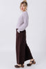 Side view of model wearing Sonnie Sweater in Mist and Atlas Pant in Chocolate, standing  in front of white wall