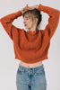 Model wearing Sonnie Sweater in Rust and light wash jeans with hands raised above head in front of white background