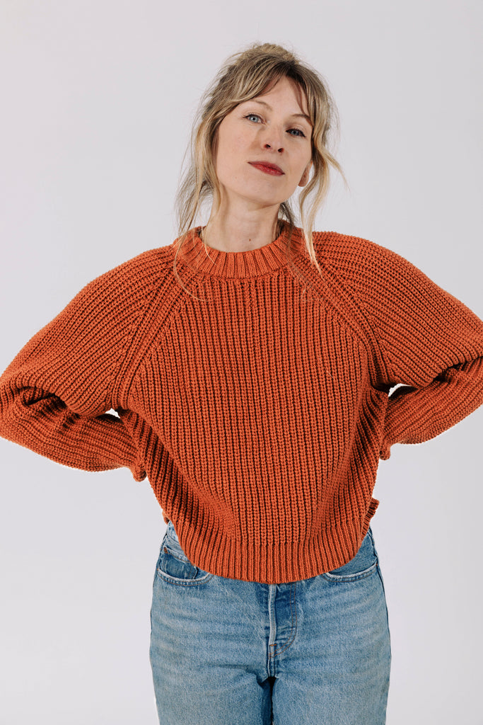 Model wearing Sonnie Sweater in Rust and light wash jeans with hands on hips in front of white background