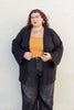 Model wearing Stevie Sweater in Black, mustard top, and black jeans in front of white wall