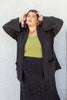 Model wearing Stevie Sweater in Black, green top, and Mae Sweater Skirt in Black in front of white wall