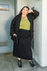 Model wearing Stevie Sweater in Black, green top, and Mae Sweater Skirt in Black in front of white wall and blue door