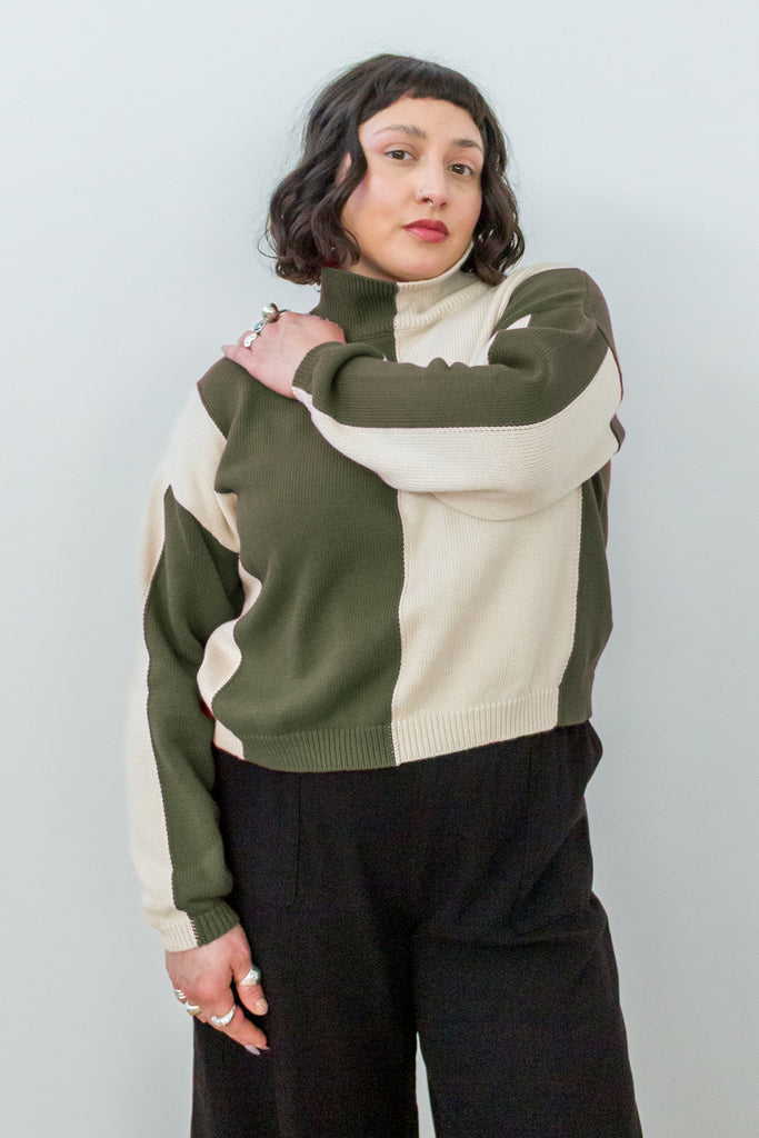 Front view of model wearing Sybil Vertical Stripe Sweater in Olive/Cream and Wide Leg Pant in black, standing with one arm across chest in front of white background