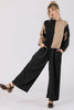 Front view of Atlas Pant in Black on model, paired with Sybil Sweater in Black/Tan, kicking a leg up in front of white background