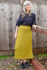 Model wearing Ayana Top in Black and Mae Sweater Skirt in Chartreuse in front of wooden wall