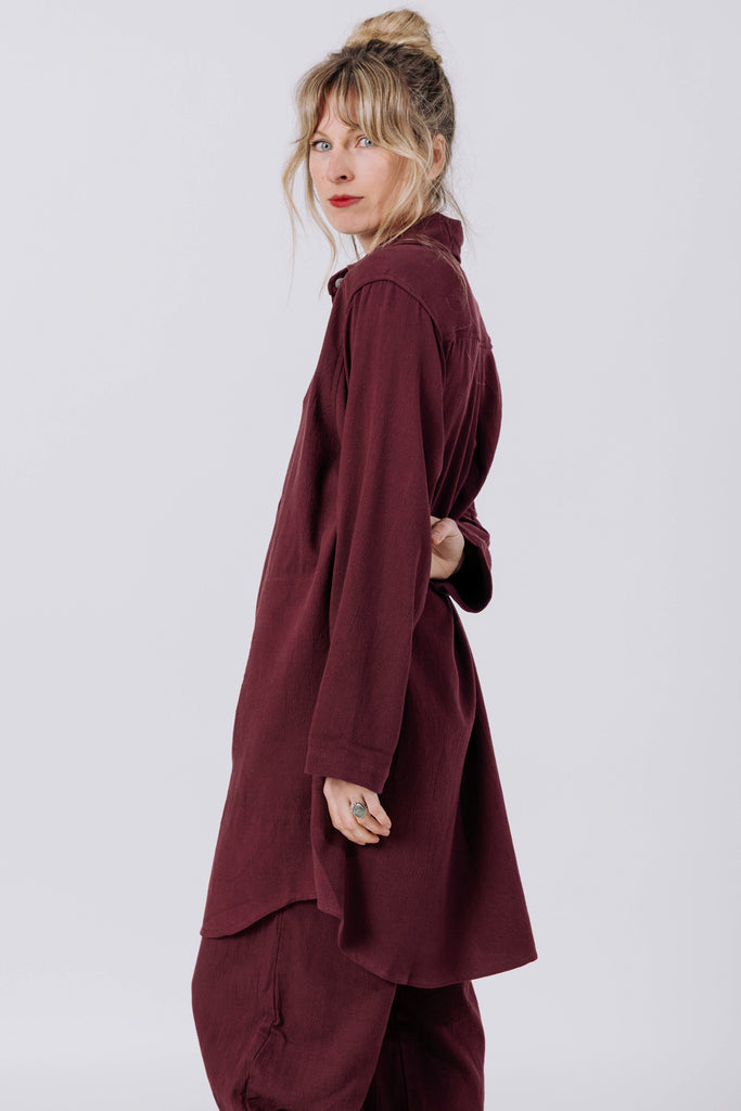 Side view of model wearing Workshirt in Burgundy and Cadence Pant in Burgundy, standing in front of white wall