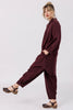 Side view of model wearing Workshirt in Burgundy and Cadence Pant in Burgundy kicking one leg out in front of white background
