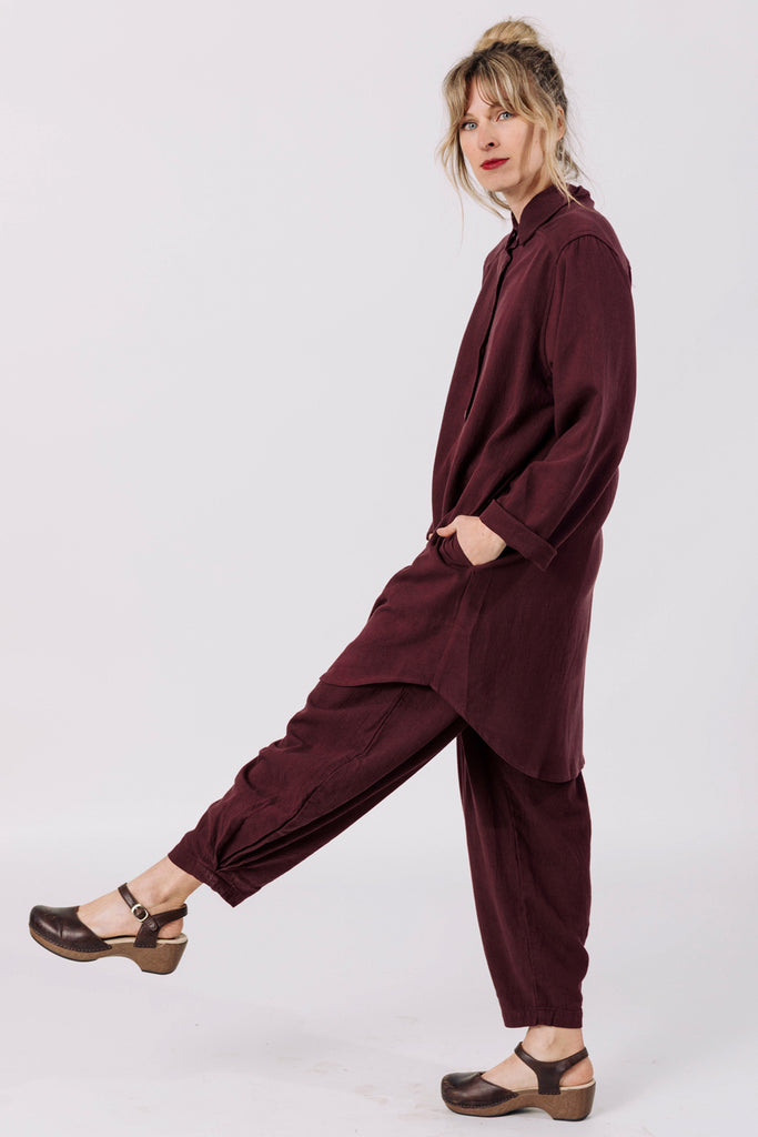 Side view of model wearing Workshirt in Burgundy and Cadence Pant in Burgundy kicking one leg out in front of white background