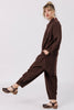 Side view of model wearing Workshirt and Cadence pants (both in Chocolate) standing with one leg kicking out in front of them, in front of white background