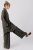 Side view of model wearing Workshirt in Mud and Atlas Pant in Mud, with hands in pockets and kicking a leg up, in front of a white background