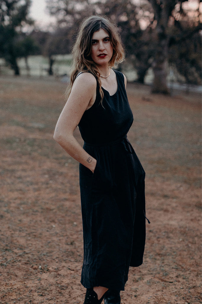 Standing model with hands in pockets of black sleeveless tie waist dress