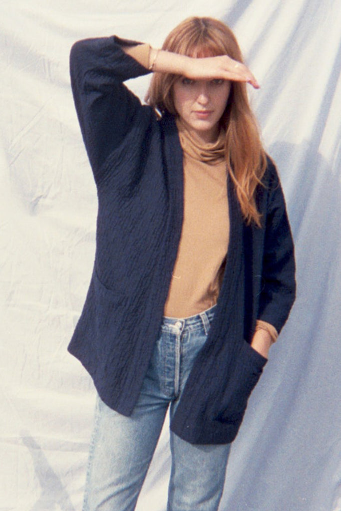 Standing model in navy blue quilted jacket, beige turtleneck, and jeans