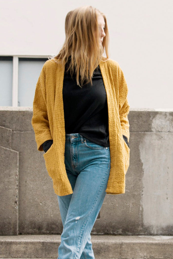 Standing model in black turtleneck, jeans and yellow textured jacket with pockets